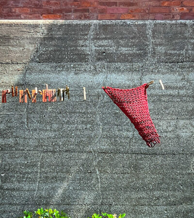 Weathered wooden clothespins on a wire against a gray stone wall with a single piece of red knitting hanging at an angle